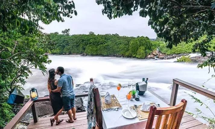 A couple relaxing on a wooden observation deck at a luxury safari lodge overlooking a scenic river in Uganda