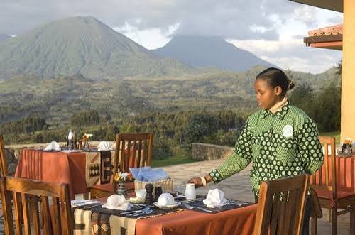 A waitress setting a table on an outdoor large terrace overlooking misty mountains in Uganda